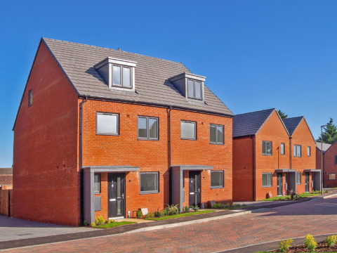 Four semi-detached red brick houses with small grass verges. A brick road is positioned in front of the house.